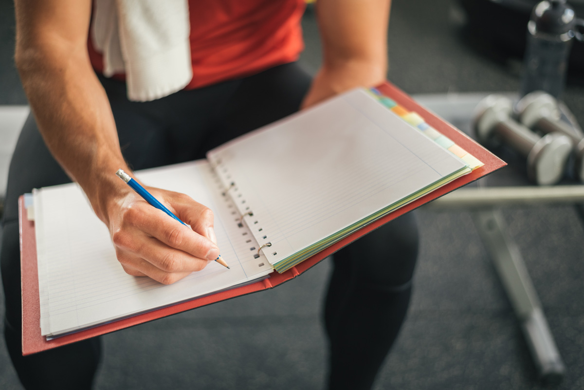 athlete strenghtening mindset by writing down muscle building goals in a three-ring binder.