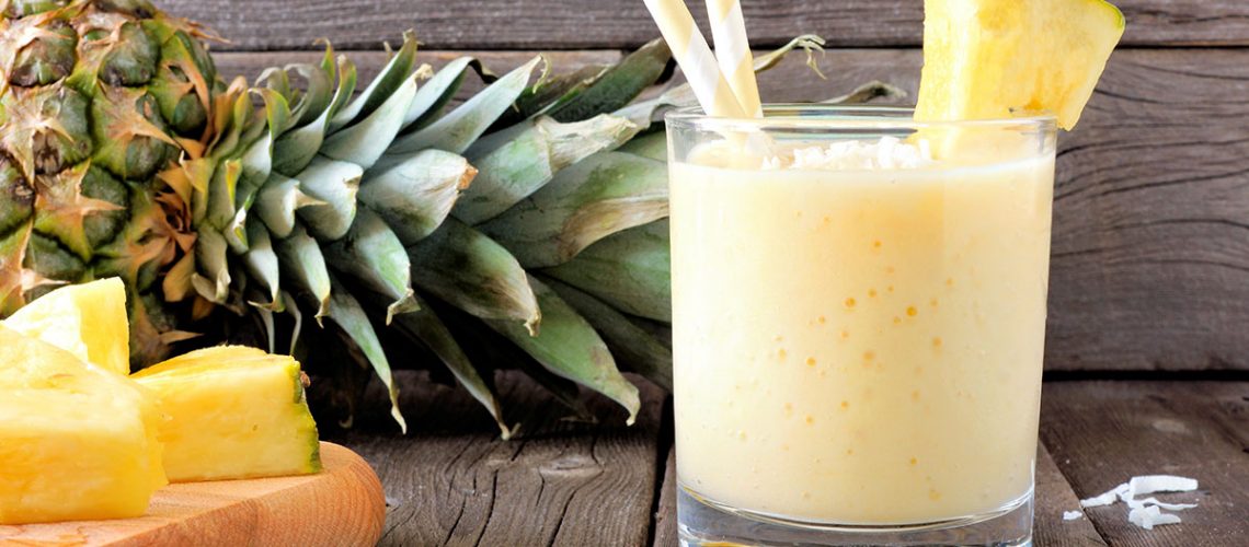 Healthy pineapple smoothie in glass, scene against an old wood background